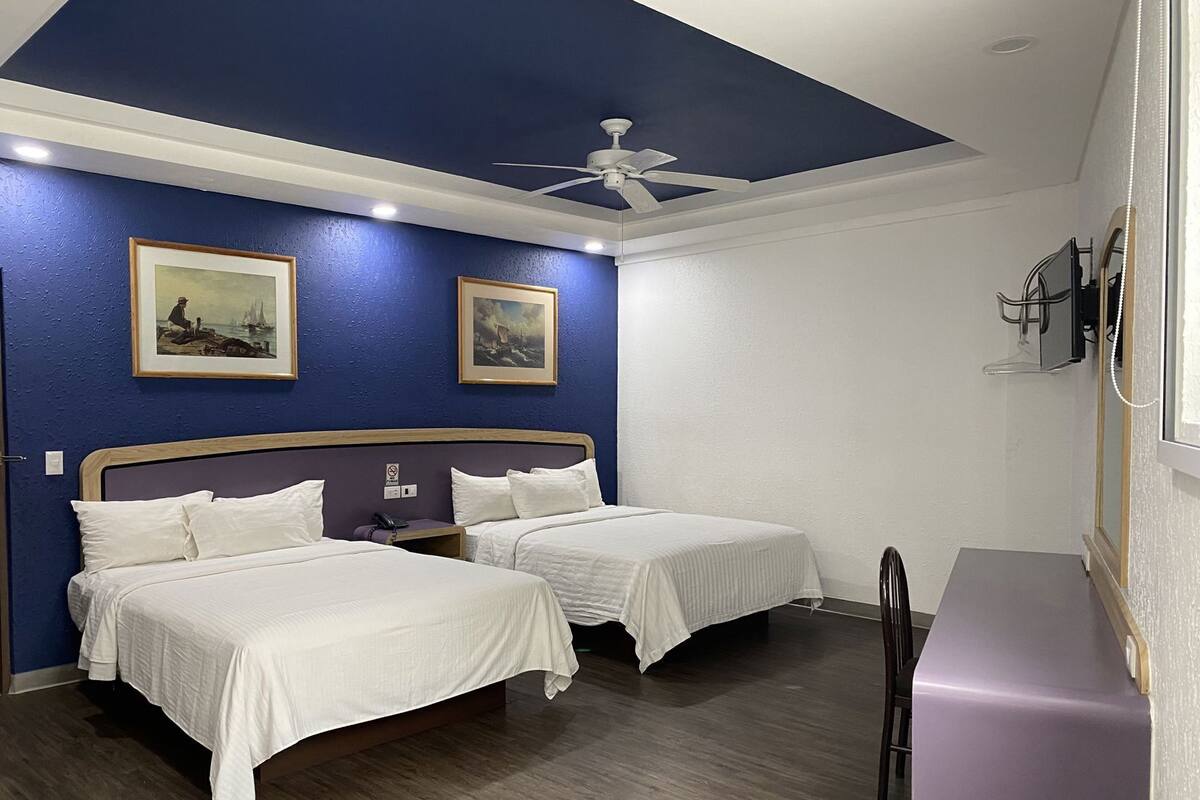 Habitación de hotel con dos camas, ventilador de techo y obras de arte en las paredes.