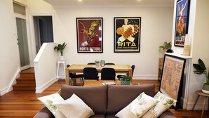 A living room with a brown sofa, two posters on the wall, a dining table with chairs, and a staircase leading to another room. - Amazing location - Walk to MCG/Swan St/Bridge Rd/Melbourne CBD (Richmond)