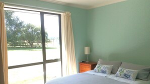 Un dormitorio con un ventanal grande, una cama con cubrecama blanco y una mesita de noche con lámpara.