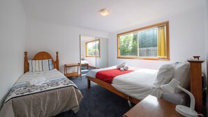 Une chambre avec deux lits simples, un bureau, une chaise, une table de chevet, une lampe et une fenêtre avec des rideaux.