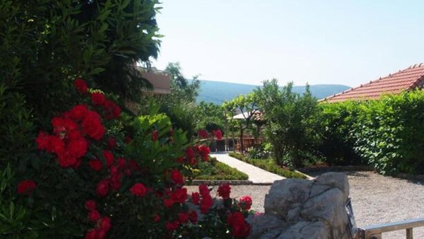 Un jardin avec des fleurs rouges et un chemin qui mène à un bâtiment doté d’un toit rouge.