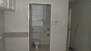 Et lille, rent badeværelse med toilet, håndvask og en glashylde over toilettet.