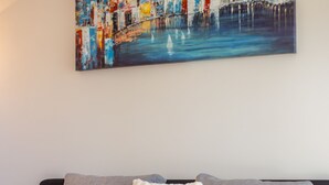 Un soggiorno moderno con un divano, un tavolino in vetro e un quadro raffigurante uno skyline urbano.