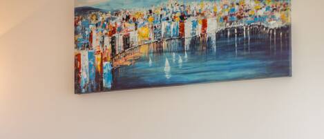A modern living room with a sofa, a glass coffee table, and a painting of a cityscape on the wall.