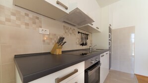 Una cucina moderna con piano di lavoro nero, mobili bianchi e forno integrato. Ci sono coltelli in un portaoggetti di legno sul piano di lavoro, e un appendiabiti con utensili sopra il lavandino.