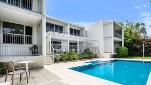 A modern building with a swimming pool, outdoor seating, and a covered patio area.