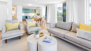 A spacious living room with a grey sofa set, a coffee table, and a dining area in the background.