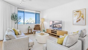 A modern living room with two grey sofas, a coffee table, a TV, and a bookshelf.