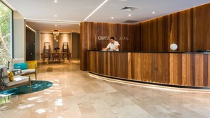 A reception area with a wooden reception desk, a seating area with a sofa and chairs, and a dining area with tables and chairs. - *LUXURIOUS* One Bedroom Condo behind Mamitas Beach (Gonzalo Guerrero)