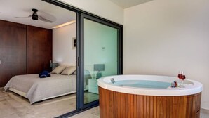 A bedroom with a bed, a wooden bathtub, and a sliding glass door leading to a bathroom. - *LUXURIOUS* One Bedroom Condo behind Mamitas Beach (Gonzalo Guerrero)