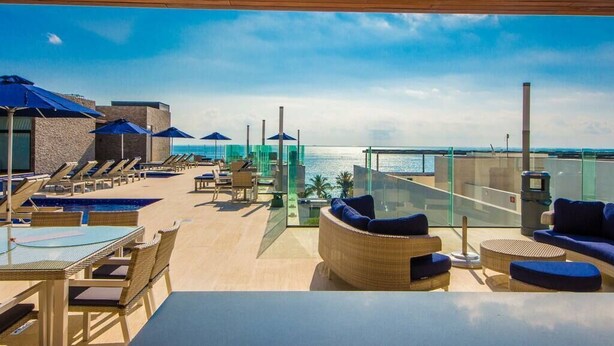 A rooftop lounge area with sun loungers, a pool, and a glass balustrade overlooking the sea. - *LUXURIOUS* One Bedroom Condo behind Mamitas Beach (Gonzalo Guerrero)