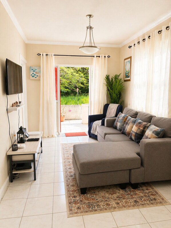A living room with a sofa, TV, and a view of greenery outside.