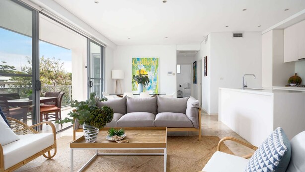 Una sala moderna con sofá, mesa de centro y sillas. Hay un balcón con vistas al exterior.