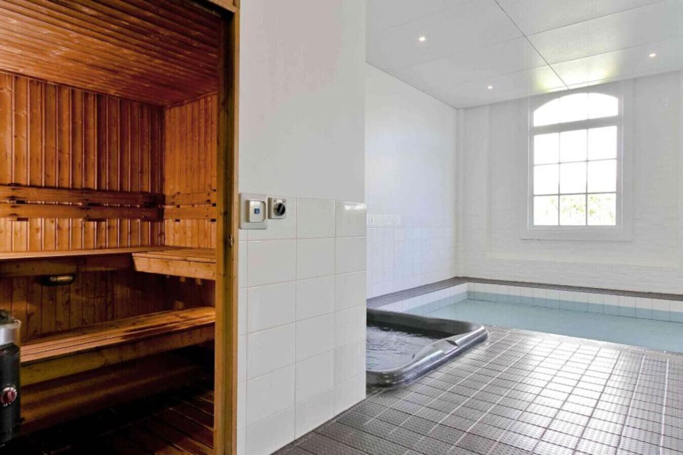 A sauna room with a wooden bench, a tiled floor, and a window.