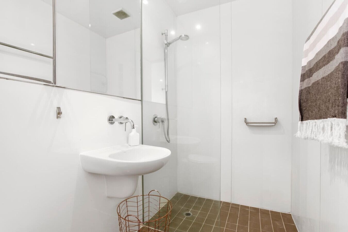 A modern bathroom with a white sink, a shower, and a towel rack.