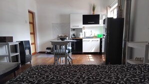 Quarto de hotel pequeno com cama, cozinha compacta, área de refeições e uma mesinha.