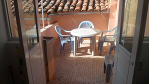 Uma pequena área de pátio com mesa e quatro cadeiras, piso e teto azulejados.