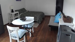 Quarto pequeno com cama, uma mesinha com uma tigela, uma cadeira, um sofá e uma televisão.