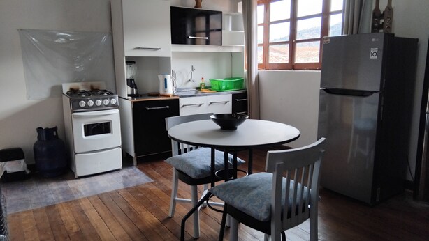 Cozinha compacta com fogão, forno e geladeira. Há uma mesa de jantar com duas cadeiras.
