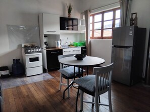 Een kleine keuken met een fornuis, oven en koelkast. Er is een eettafel met twee stoelen.