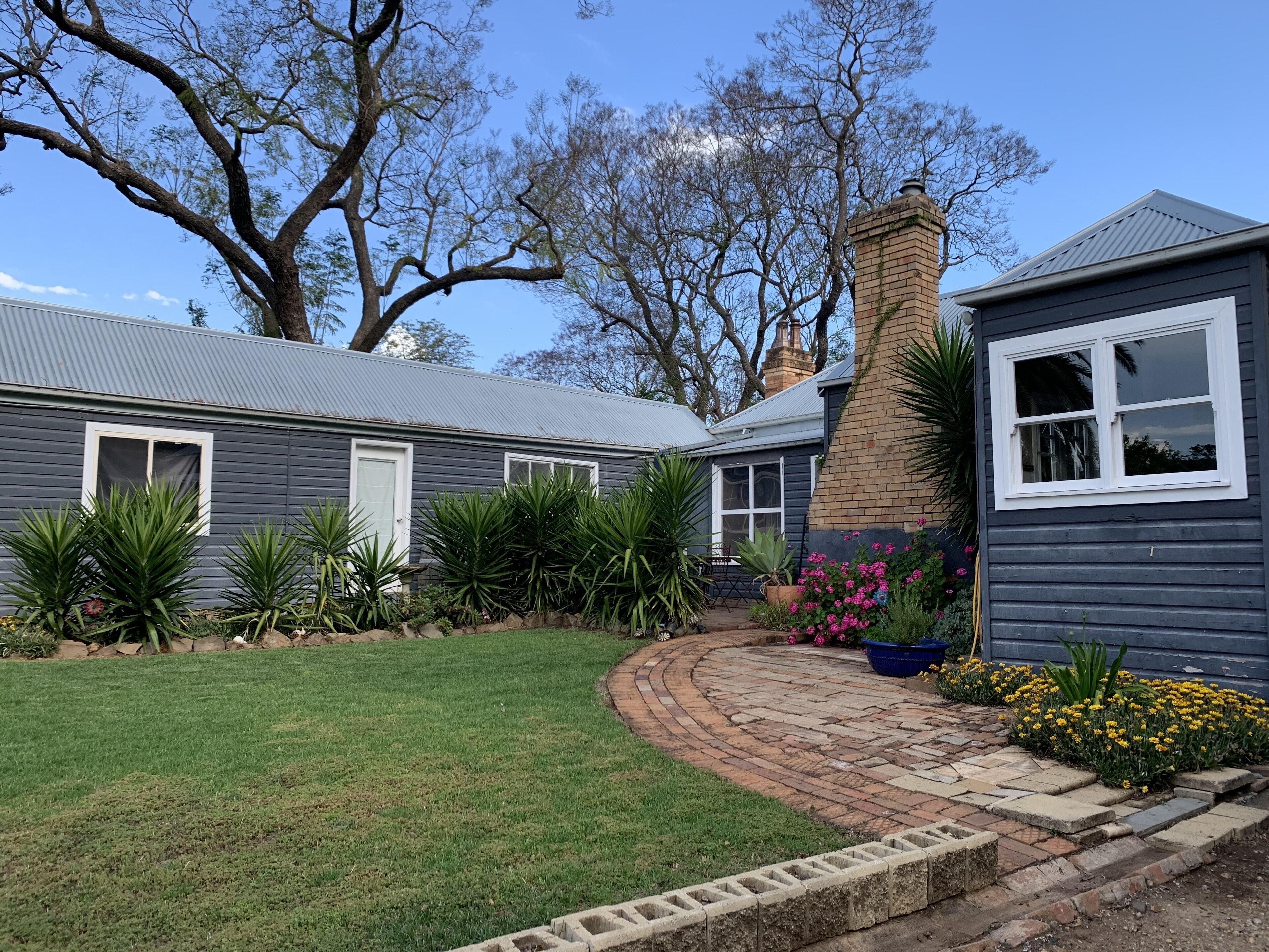 A residential property with a grey house, a brick chimney, and a garden with various plants and flowers.