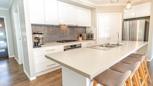 Eine moderne Küche mit weißen Schränken, einem Edelstahlkühlschrank und einer großen Kücheninsel mit Barhocker.