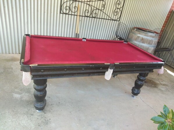 Una mesa de billar con superficie de fieltro rojo, patas negras y estructura metálica.