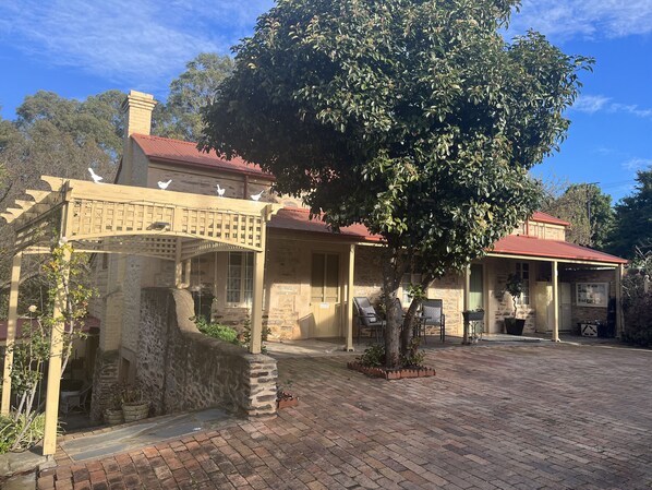 A stone building with a red roof, a covered porch, and a brick courtyard.