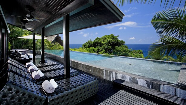 An infinity pool with a view of the ocean, lounge chairs with towels, and a covered seating area. - Villa Yang-5 BR Luxury Villa(Butler,Chef,Transfer) (Kamala)