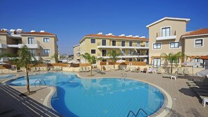 Una piscina circondata da edifici a più piani con balconi, un cielo azzurro limpido e alcune palme.