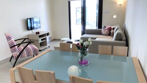Un soggiorno moderno con un tavolo da pranzo in vetro, una poltrona a righe, un divano con cuscini decorati, una TV a parete e un vaso con fiori sul tavolo.