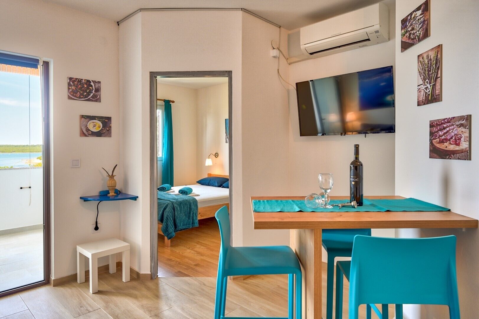 A room with a bed, a TV mounted on the wall, a table with chairs, and a window with a view.