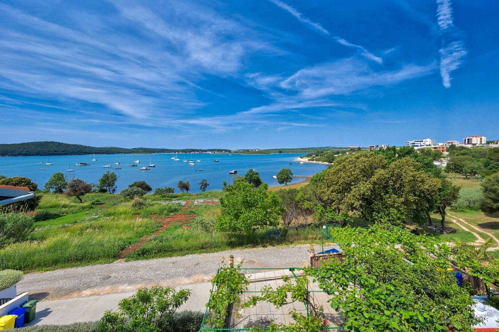 A coastal view with boats on the water, greenery, and buildings in the background.