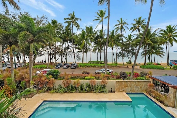 A pool with a view of palm trees and a road with parked cars.