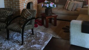 A living room with a brick fireplace, a chandelier, a sofa, and striped chairs. - Vacation home 4 Palmeiras  (Figueira)