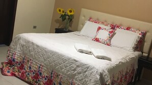 A neatly made bed with a floral quilt, a bedside table with a vase of sunflowers, and a headboard with floral pillows. - Vacation home 4 Palmeiras  (Figueira)
