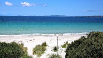 A beach with clear blue water, a sandy shore, and a sign indicating no swimming.
