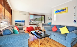 A living room with a blue sofa, a red bean bag, and a black coffee table. There is a window with blinds, a globe on a small table, and a painting on the wall.