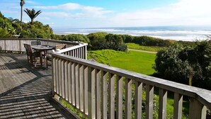 A wooden deck with a table and chairs overlooking a grassy area and the ocean. - Home by the Beach with sensational view! Pet-friendly. (Westport)