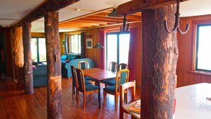 A rustic cabin interior with wooden beams, a dining area with a table and chairs, and a cozy seating area with cushions. - Home by the Beach with sensational view! Pet-friendly. (Westport)