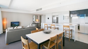 Une chambre d’hôtel moderne dotée d’un coin repas, d’un canapé, d’une télévision et d’un espace cuisine.