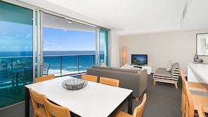 Une chambre moderne dotée d’un balcon avec vue sur l’océan, d’un coin repas et d’un espace salon avec un téléviseur.
