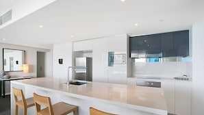 Une cuisine moderne dotée d’un grand îlot central, d’appareils électroménagers en acier inoxydable et de chaises en bois.