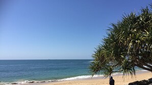 En strand med en person siddende på en klippe, der ser ud over havet.