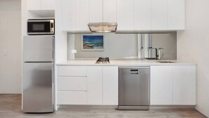 A modern kitchen with white cabinetry, a stainless steel refrigerator, a microwave, a dishwasher, and a gas stove.