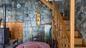 Ein Zimmer mit Steinwänden, einer Holztreppe, einem Holztisch und einer rot gemusterten Tischdecke.