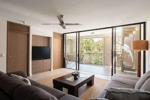 A modern living room with a flat-screen TV, a ceiling fan, a sofa, a coffee table, and a sliding glass door leading to a balcony.