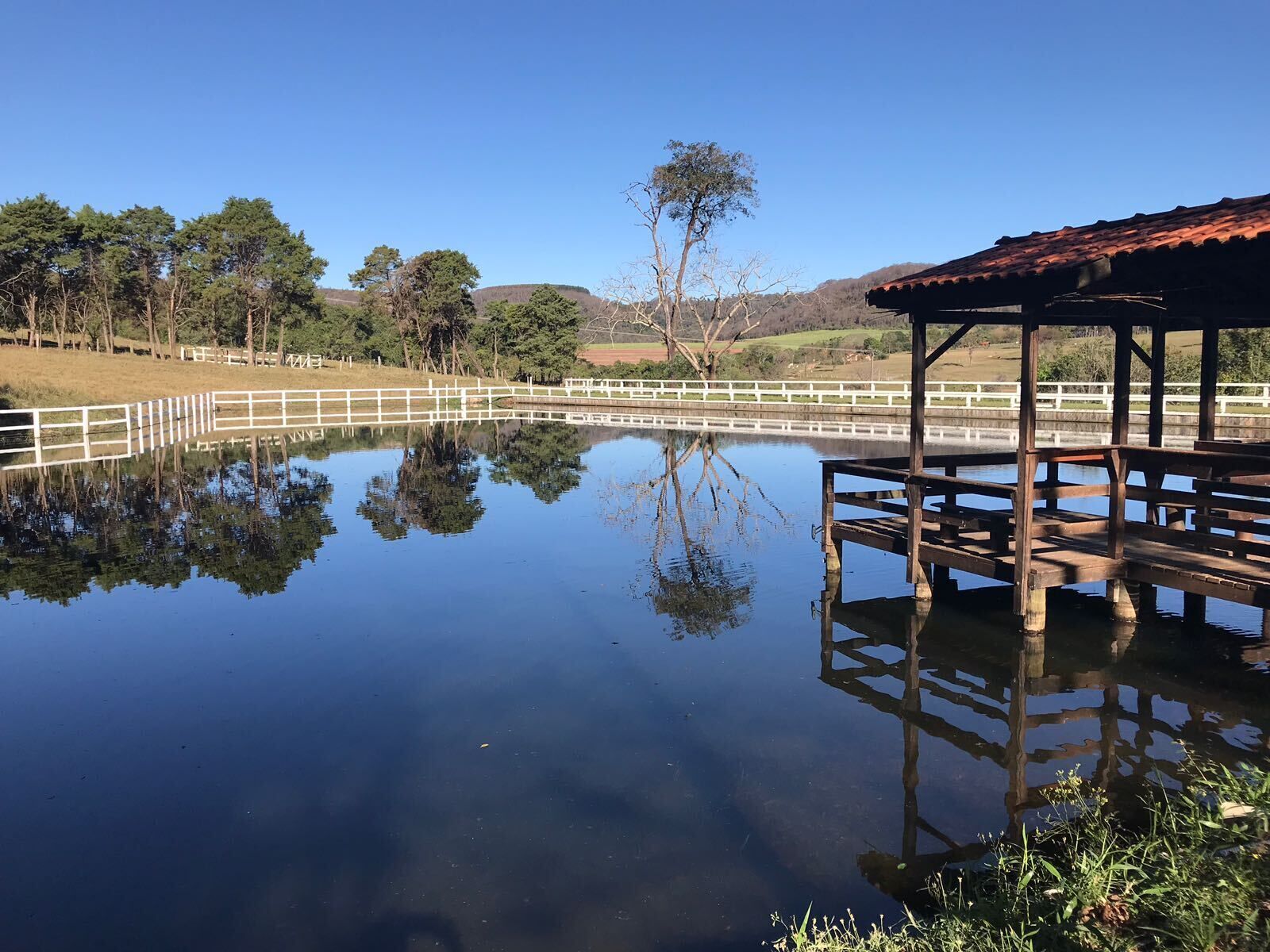 A tranquil outdoor area with a wooden deck and a white fence surrounding a calm body of water.