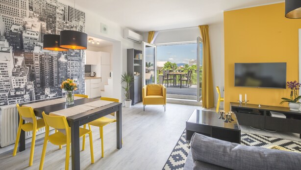A modern living room with a dining area, a sofa, a TV, and a cityscape mural.
