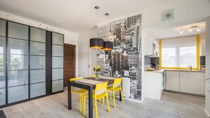A modern kitchen with a cityscape mural, a dining area with yellow chairs, and a sliding glass door leading to an outdoor area.